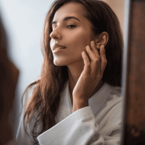 Woman looking into a mirror touching her masseter muscle.