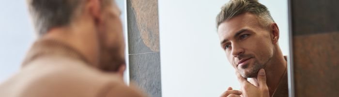 Man looking into the mirror touching his chin